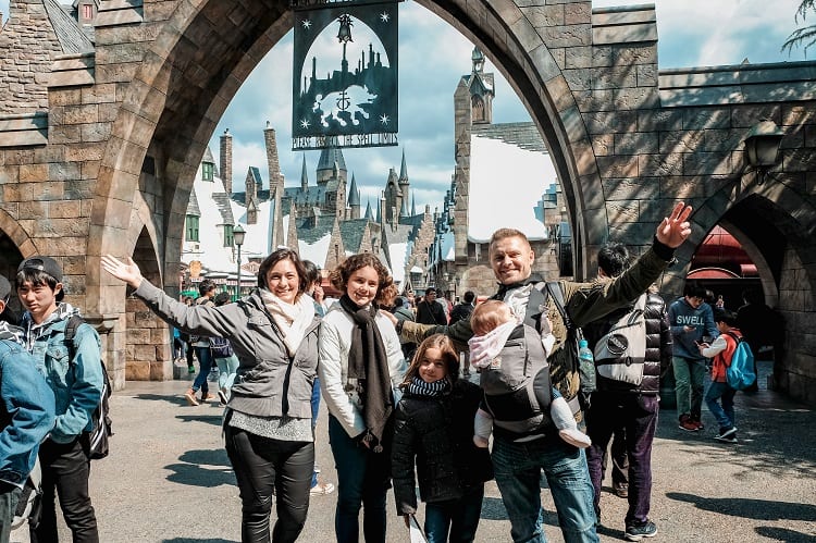 family standing before an archway to Harry Potter town in Universal Studios in Japan, baby in the baby carrier