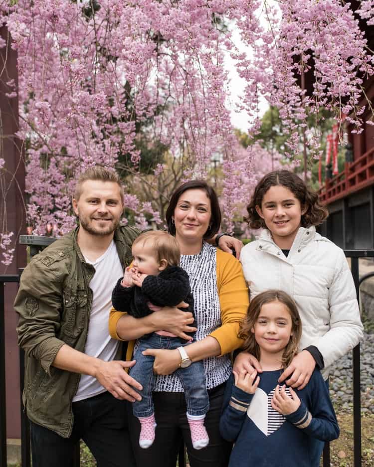 Family posing for a photo in front of Pink Cherry Blossom trees, smiling, dressed in warm clothes
