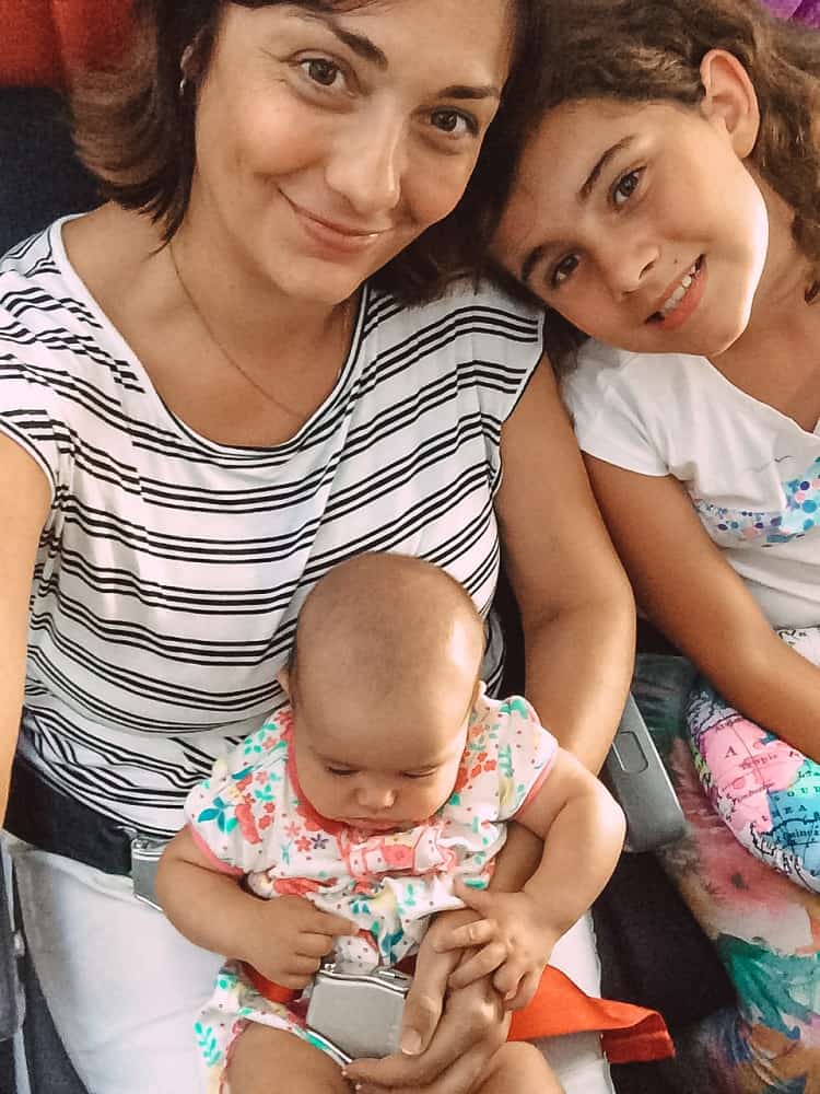 mother and two daughters, including one baby, sitting in the airplane, smiling