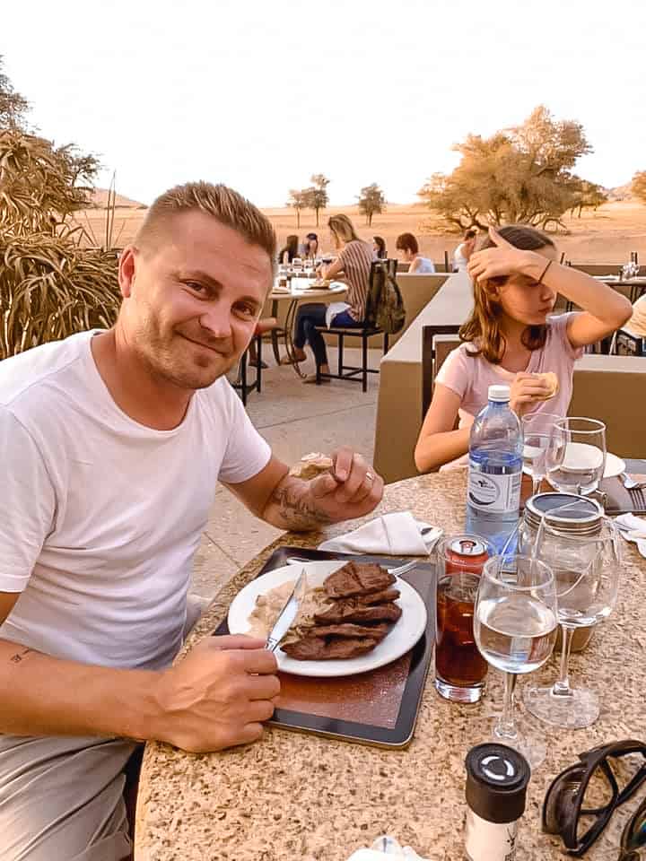 Dining in Namibia Sossusvlei, father and daughter eating dinner steak in a restaurant, desert in background