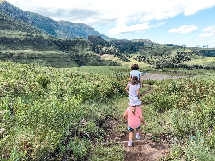 Drakensberg Mountains in South Africa, three young girls walking on the pathway in the national park, green grass, mountains