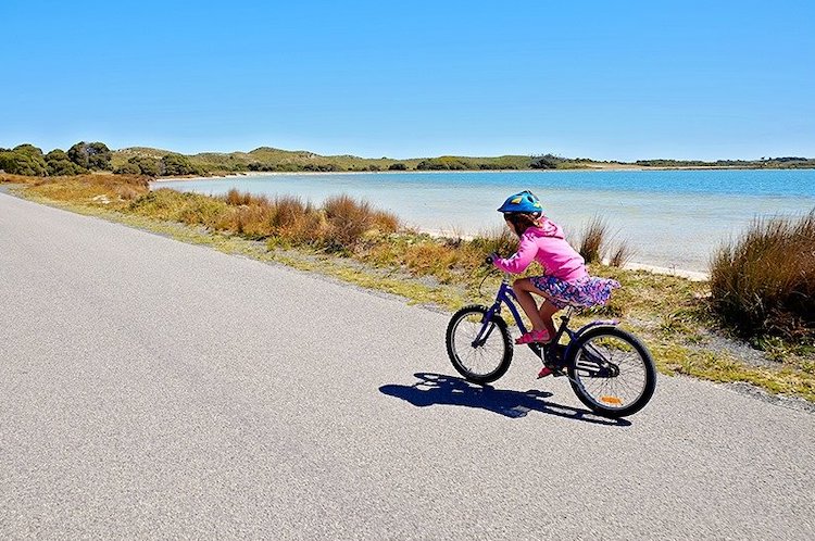 Girl riding a bicycle on the road in Rotnests Island, Western Australia, 