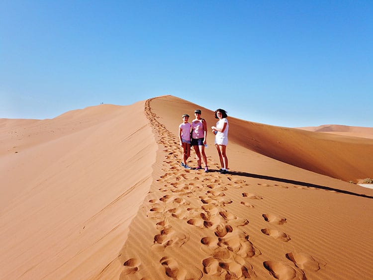 Mother and two daughters standing on the ridge of the sand dune in Soussusvlei in Namibia