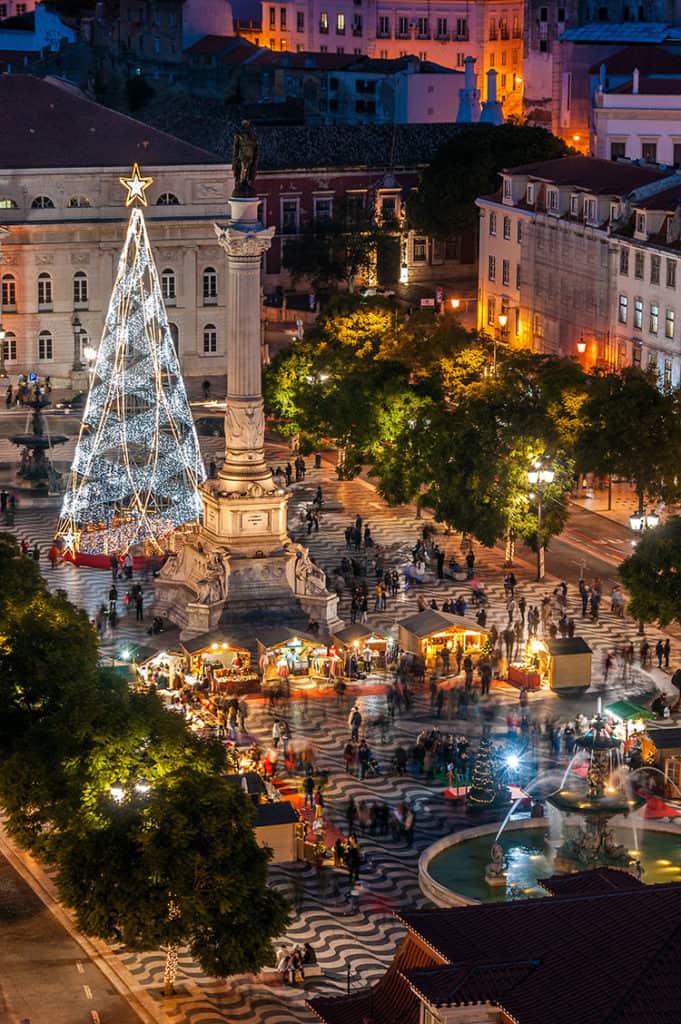 Lisbon, Portugal, Christmas tree lit up with Christmas lights in the square, monument and markets at night, people walking around