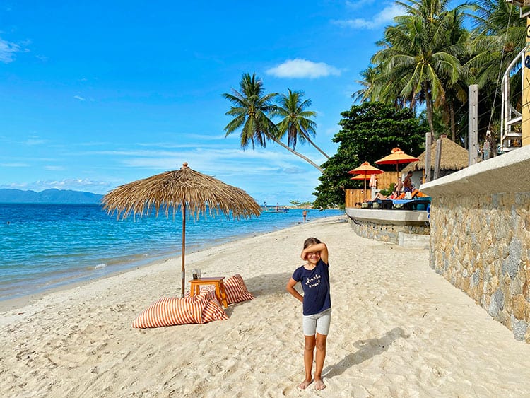 Beautiful Ban Tai Beach in koh Samui, Thailand, young girl standing on the beach, palm trees, straw umbrella and bean bags on the beach