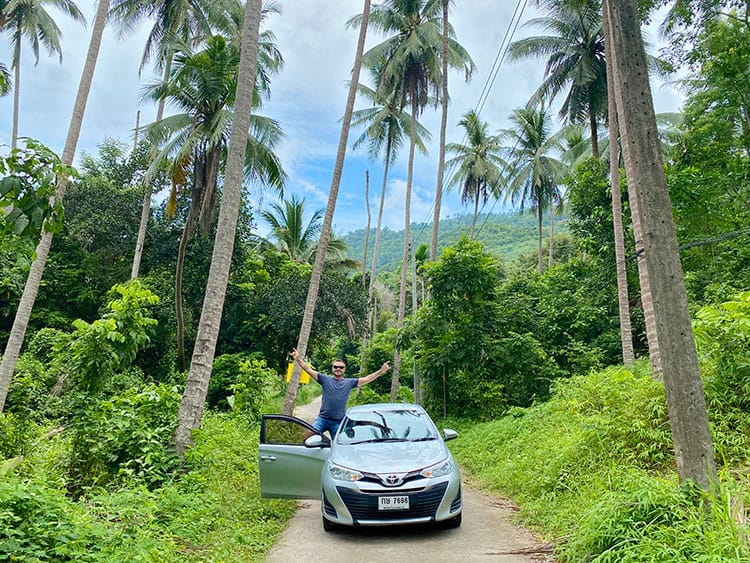Koh Samui, Thailand, man posing with the car on a small road in the palm tree forest