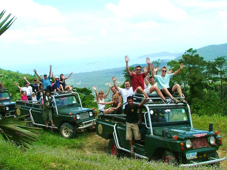 Jeep safari in Koh Samui, Thailand, tourists sitting on the tops of Jeeps, arms up, three green Jeep cars