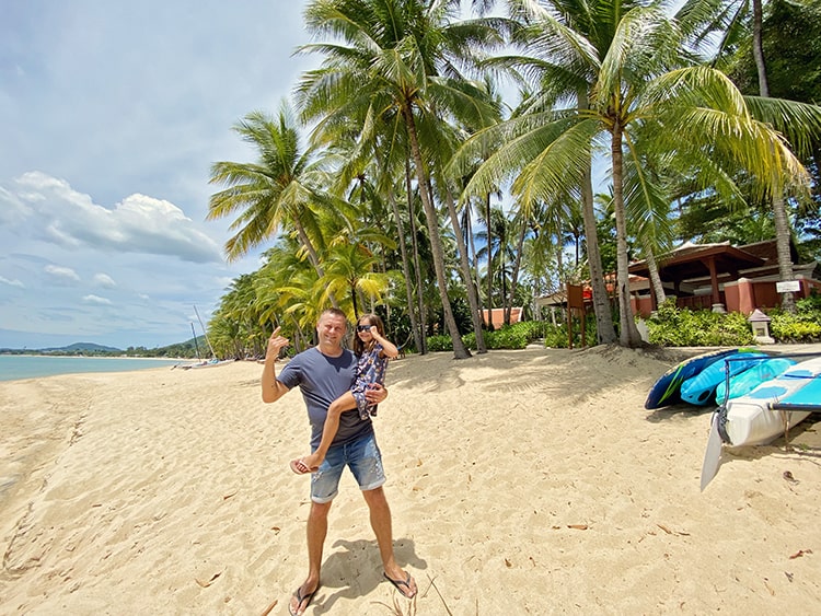 Maenam Beach Koh Samui, Thailand, father holding the young daughter on his arm, palm trees, kayaks