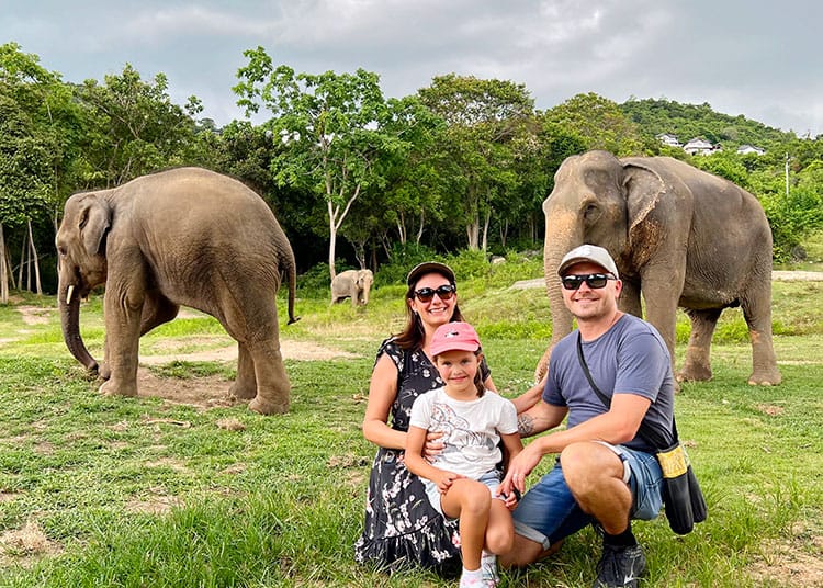 Samui Elephant Haven Visit, Koh Samui, Thailand, family crouching in front of the three elephants, two adult elephants, one baby elephant