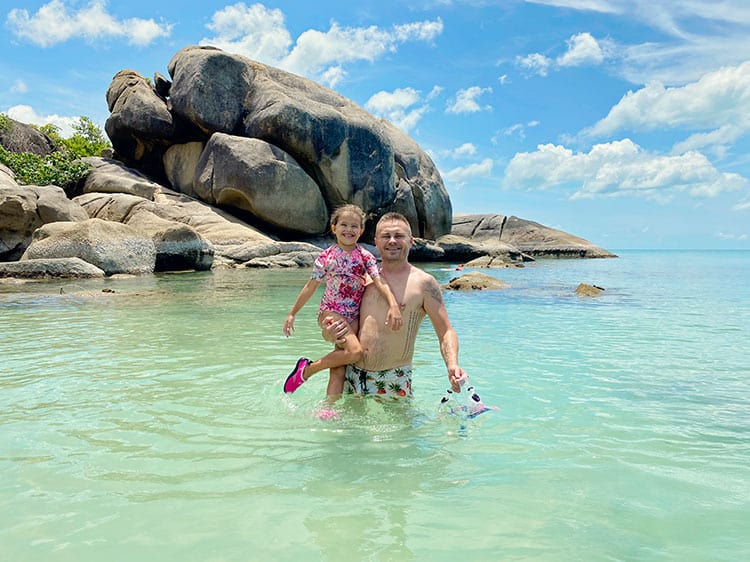 Snorkeling at Silver Beach Koh Samui, Thailand, father and daughter in standing in the water, rocks in background