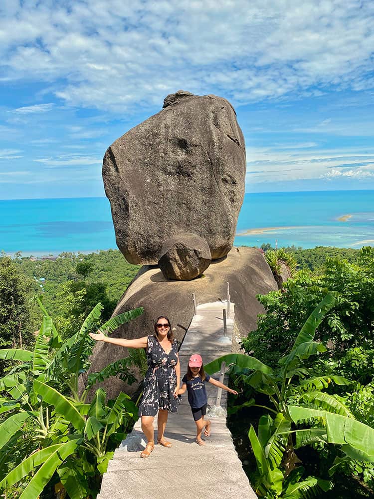 Things to do in Koh Samui see Overlap Stone, Thailand, mother and daughter standing on a bridge, rock in the background, ocean far away