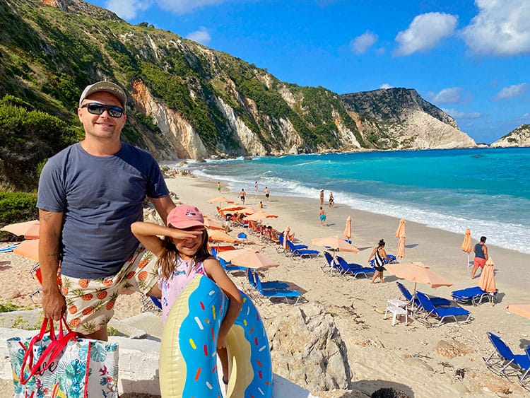 Petani Beach, Kefalonia, Greece, Things to do in Kefalonia, father and daughter standing with beach in background, rocky shore, beach chairs, umbrellas