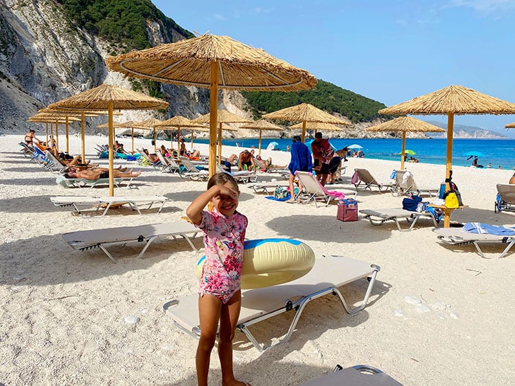 Myrtos Beach, Things to do in Kefalonia, Greece, young girl at the beach, sun loungers, beach umbrellas, tourists