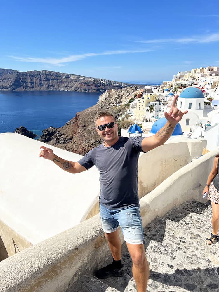 Santorini Greece, man standing with arms up with the blue dome and white city of Oia behind