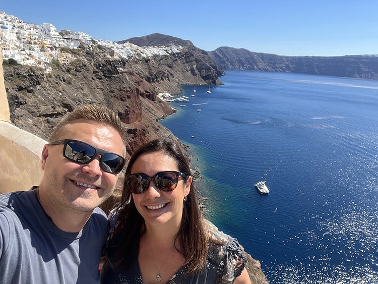 Santorini in September, Greece - man and woman selfie with Oia town on top of the rocky shore in the background