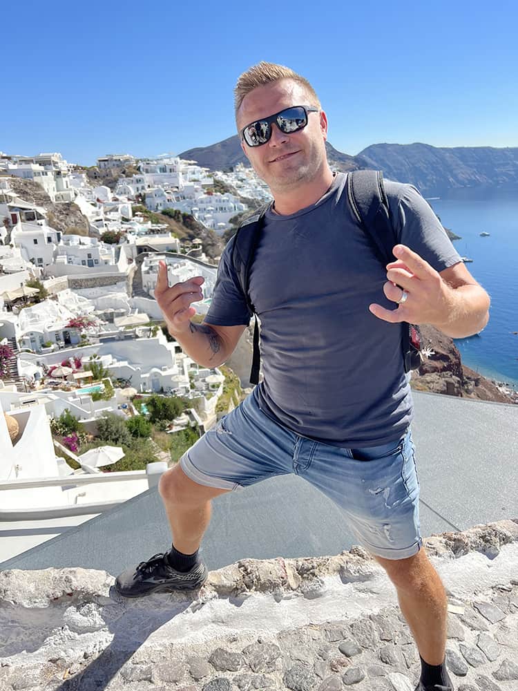 Santorini in September, Greece - man posing arms up, view of the Oia old town in background
