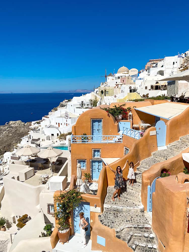 Santorini in September, Greece - mother and daughter posing in front of buildings, orange and white buildings