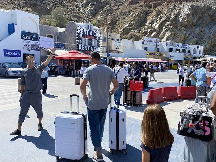 Santorini in September, Greece - people with luggage, people walking, car hire and other shops in background