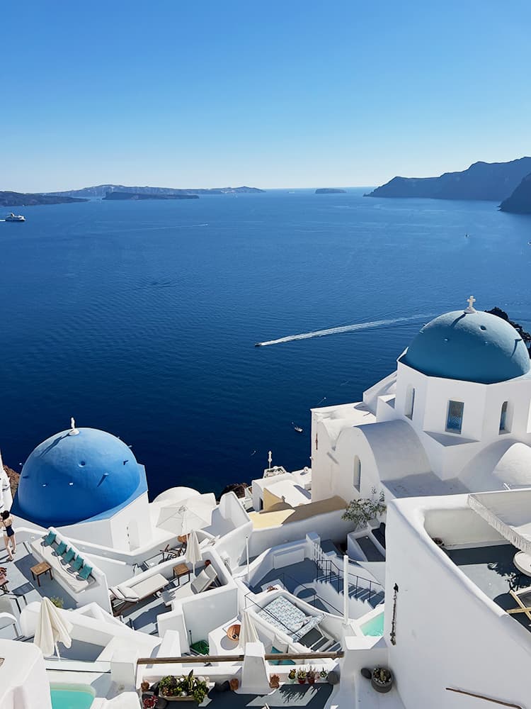 Santorini in September, Greece - white buildings in Oia, Blue domes, water, boat