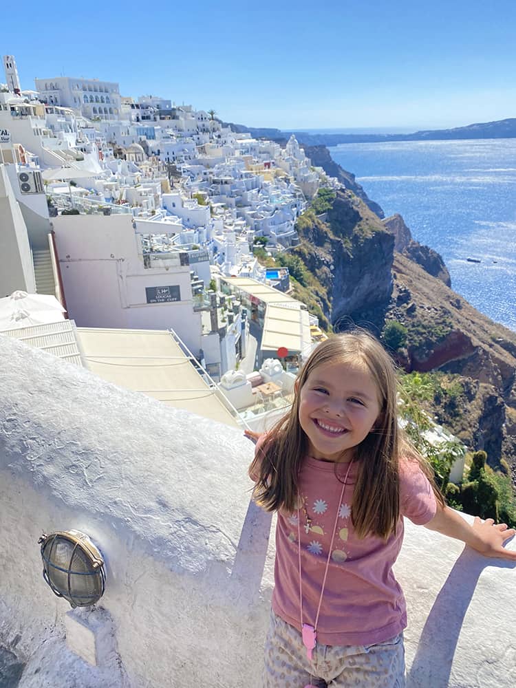 Santorini in September, Greece - young girl posing at with the view of Thira town on the side of the mountain